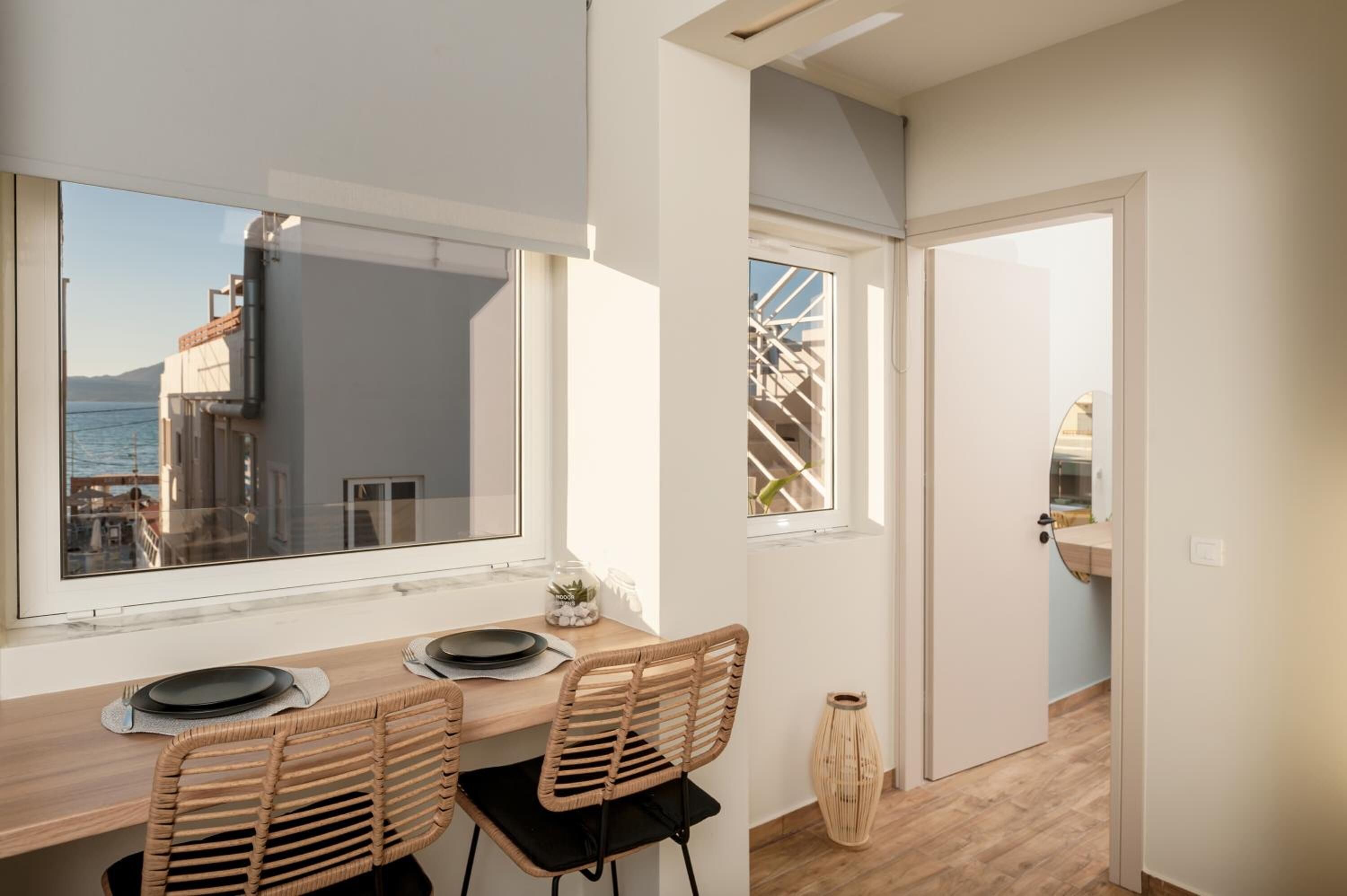 A modern kitchen with a dining area, large windows with a view of the sea, and a wooden floor.