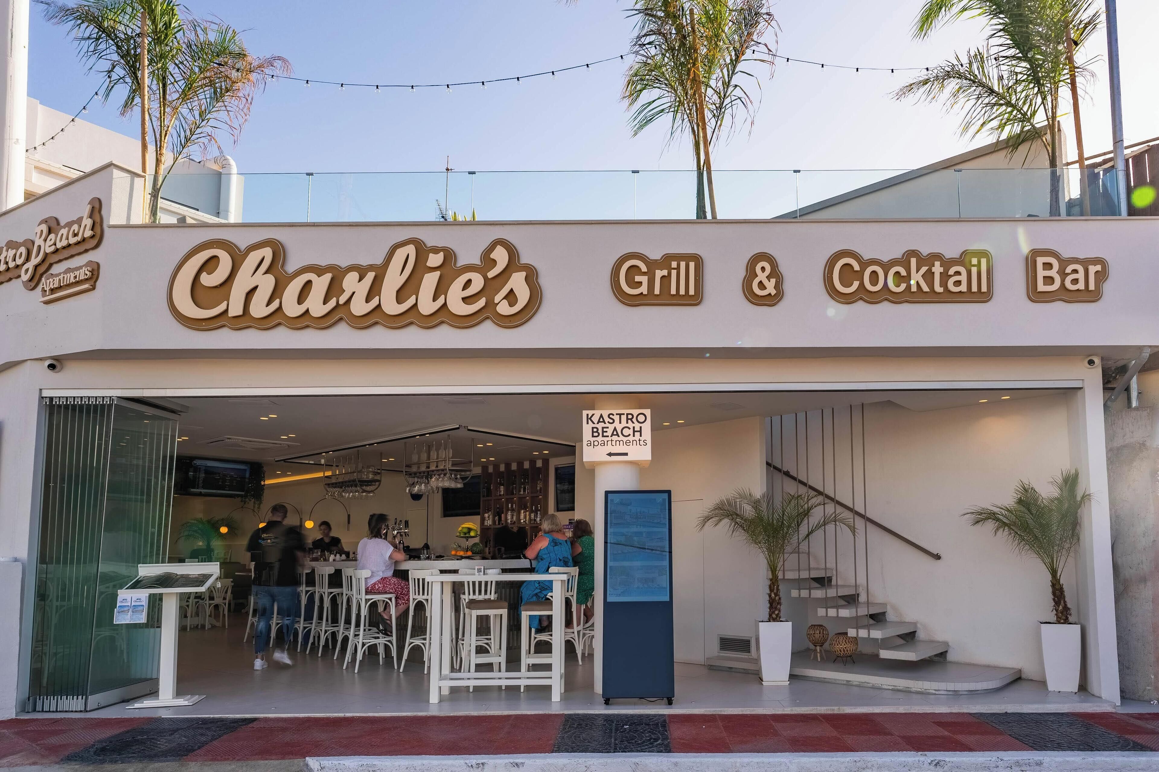 Charlie's Grill & Cocktail Bar, med uteservering, och en skylt som visar vägen till Kastro Beach Apartments.