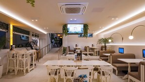 Een modern café met witte meubels, een groot televisiescherm en kamerplanten.