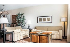 Relax in this inviting living room with a beige sofa, coffee table, and floor lamp, surrounded by artwork and a potted plant.