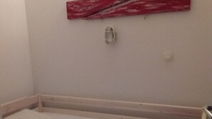 A single bed with a white mattress and red pillows, a small bedside table, and a wall-mounted light fixture. - Résidence la Goyave (Biscarrosse de la plage)
