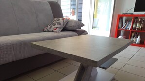 A modern living room with a grey sofa, a grey table with a unique base, and a red bookshelf in the background. - Résidence la Goyave (Biscarrosse de la plage)