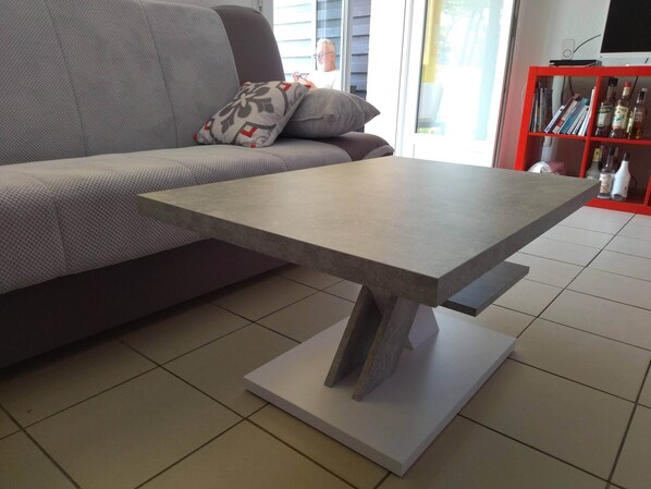 Una sala de estar moderna con un sofá gris, una mesa gris de diseño y una estantería roja al fondo.