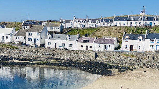 A coastal town with white houses, a sandy beach, and a rocky shoreline.