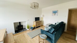 A modern living room with a blue sofa, wooden flooring, a fireplace, a television, and a lamp.