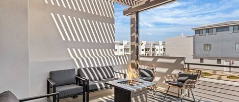A rooftop terrace with a fire pit, outdoor seating, and a view of the cityscape.