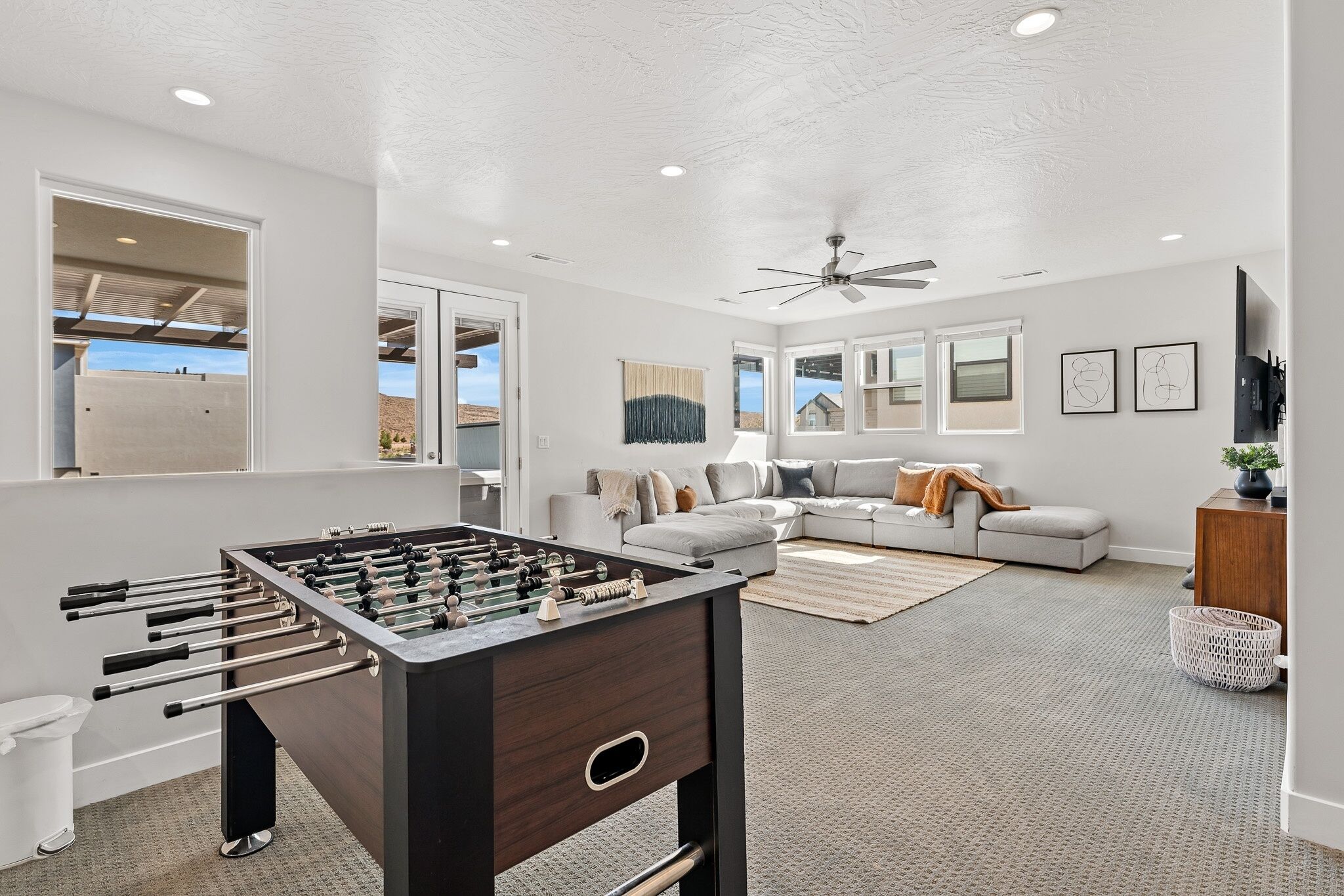 A modern living room with a foosball table, a gray sofa, and a ceiling fan.