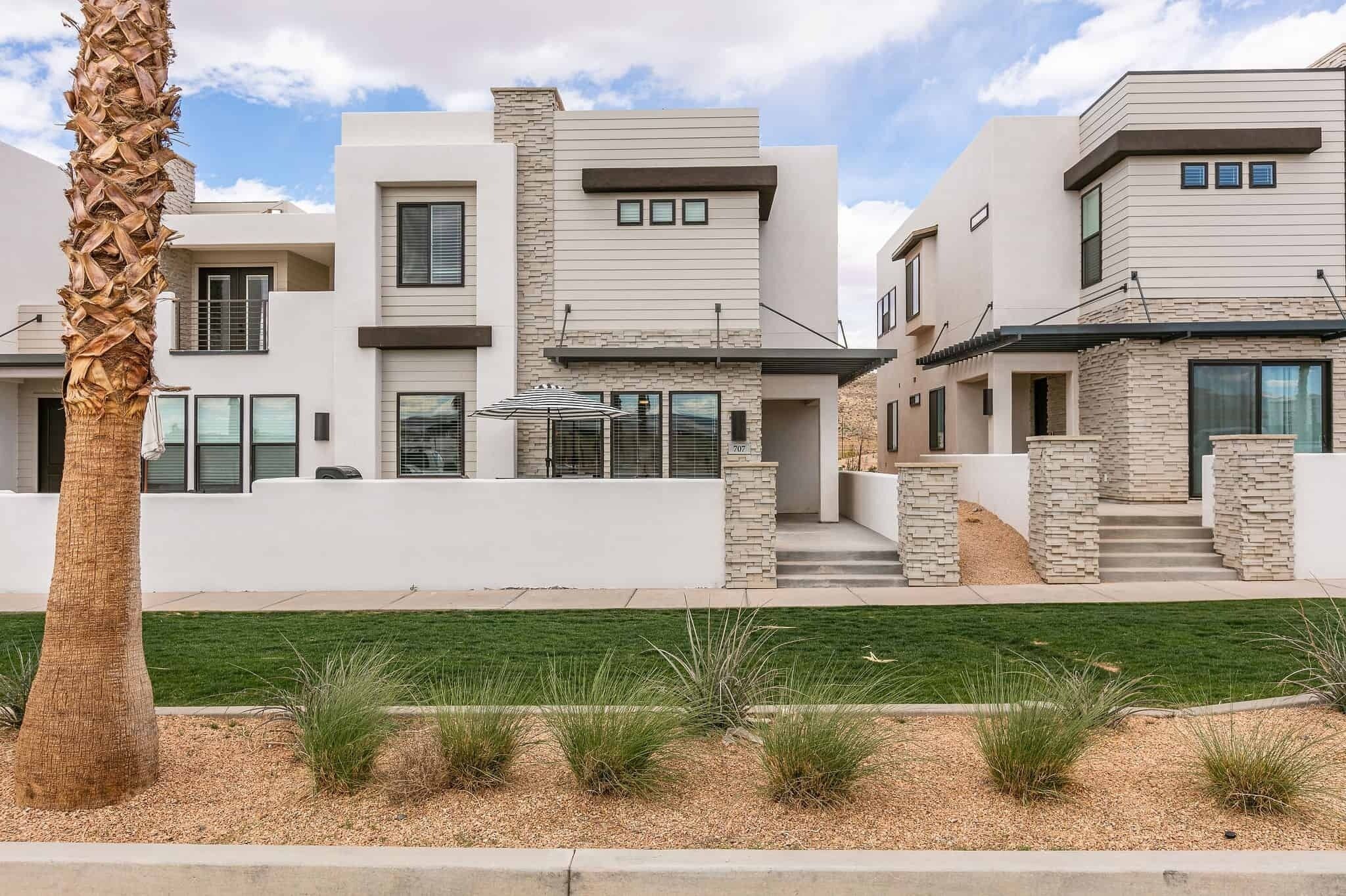 A modern two-story house with a stone facade, a well-maintained lawn, and a palm tree.
