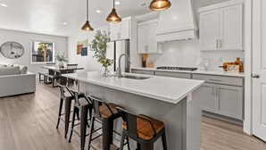 Een moderne keuken met witte kastjes, een groot eiland met barstoelen, hanglampen en uitzicht op het omliggende landschap.