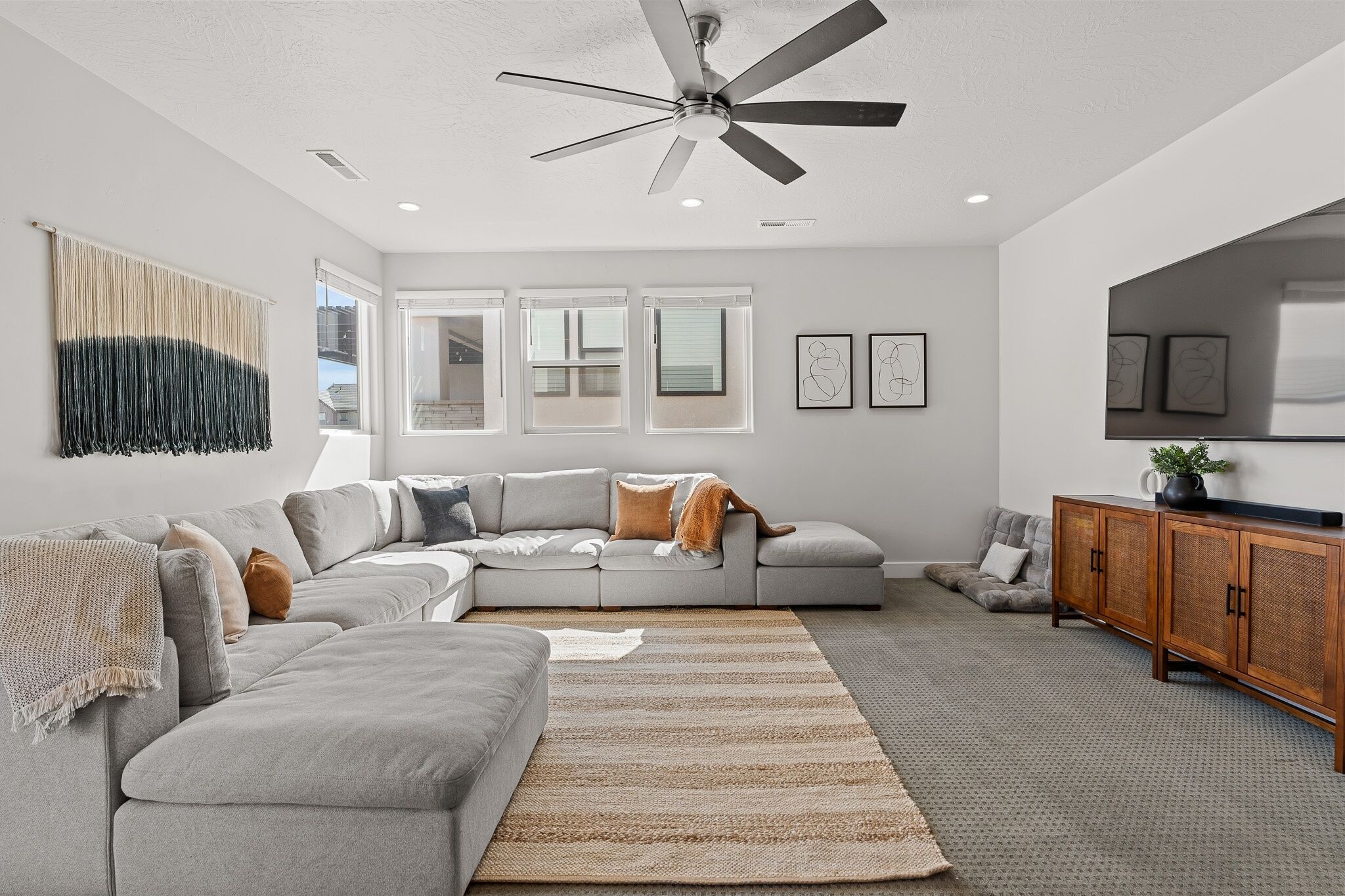 Un salon moderne avec un canapé d’angle gris, un meuble en bois et un ventilateur de plafond.