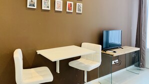 A modern room with a brown wall, a white table, two white chairs, and a TV on a glass stand.