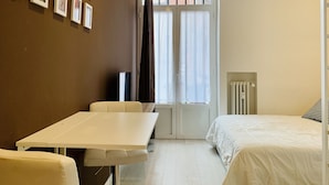 A room with a bed, a table, and a TV. There are curtains on the window, and an air conditioner is mounted on the wall.