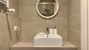 A bathroom with a rectangular sink, a round mirror, and a towel dispenser.