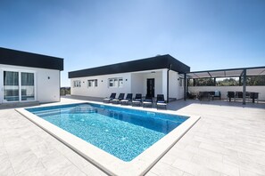 A modern outdoor swimming pool with lounge chairs and a covered seating area. - Villa Vallelunga  (Pula)