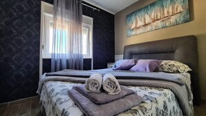 Een slaapkamer met een bed, een raam met gordijnen, een schilderij aan de muur en een hoofdeinde.