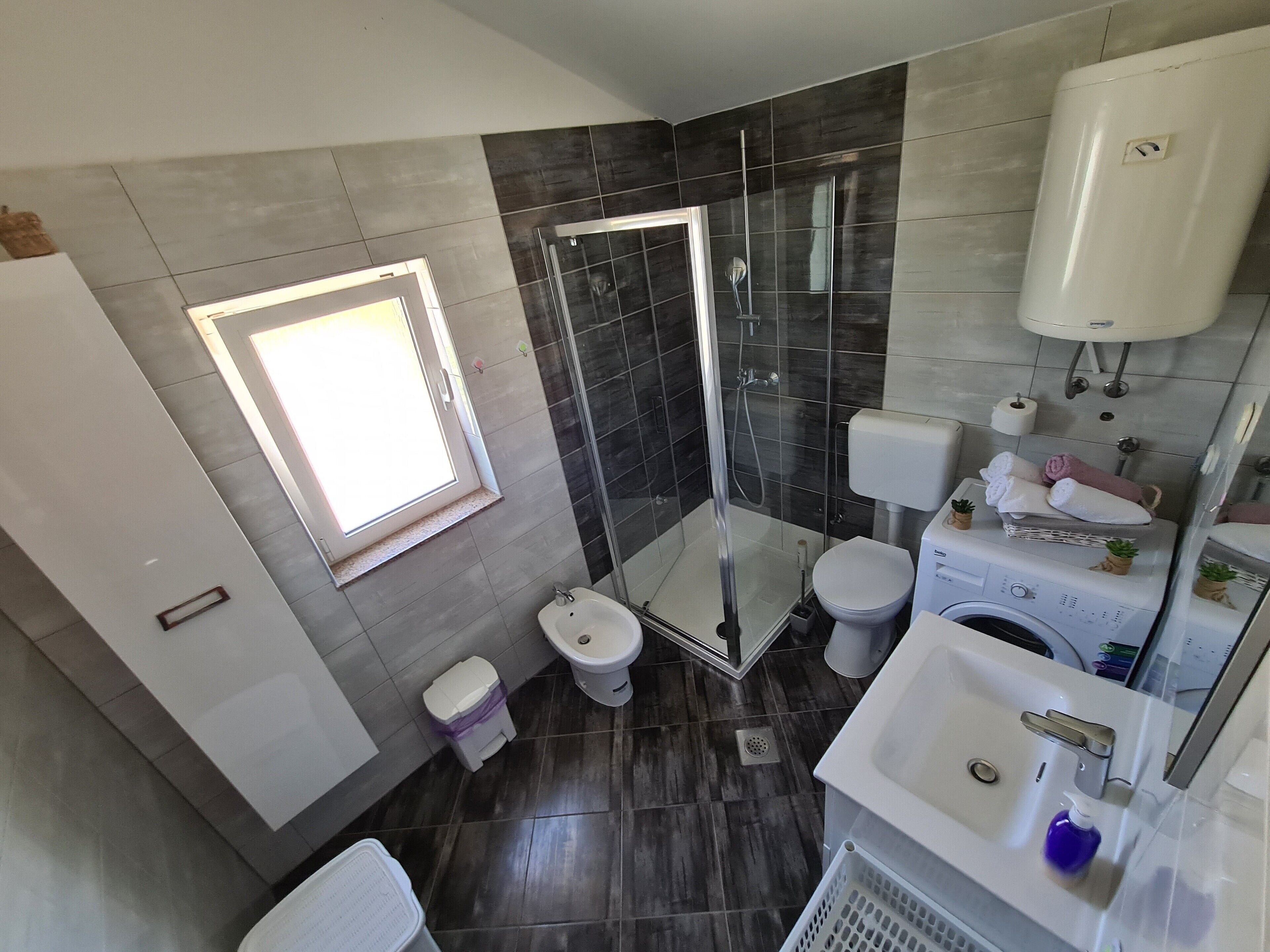 Une salle de bain moderne dotée d’une douche à parois de verre, de toilettes, d’un lavabo et d’une fenêtre laissant entrer la lumière naturelle.