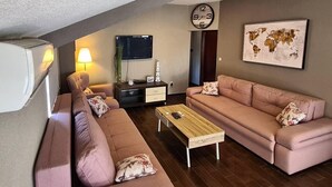Een woonkamer met twee banken, een salontafel, een televisie, een klok en een wereldkaart aan de muur.