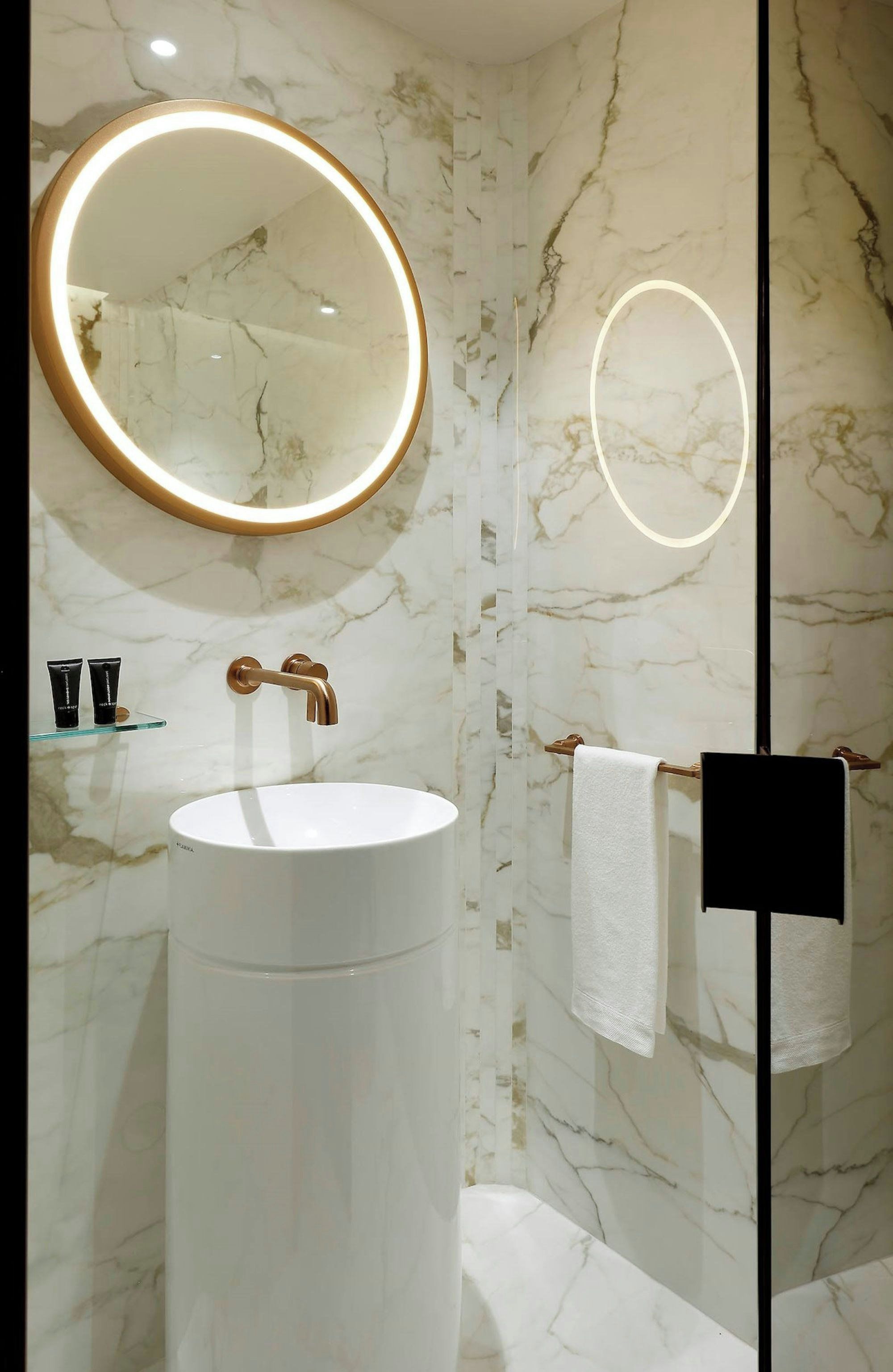 Un baño con un espejo redondo, un lavabo y un perchero para toallas.
