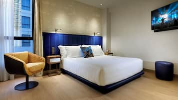 Habitación de hotel moderna con una cama grande, una mesita de noche, una silla y un televisor fijado a la pared.