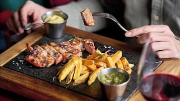 Una tabla de madera con carne a la parrilla, papas fritas y salsas.