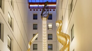 Een ruime hotellobby met een centraal spiraalvormig lampenarmatuur, comfortabele zithoeken en een helder uitzicht op de hogere verdiepingen.