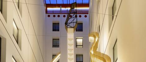 Un amplio vestíbulo de hotel con una lámpara espiral central, zonas de estar confortables y vistas despejadas a los pisos superiores.