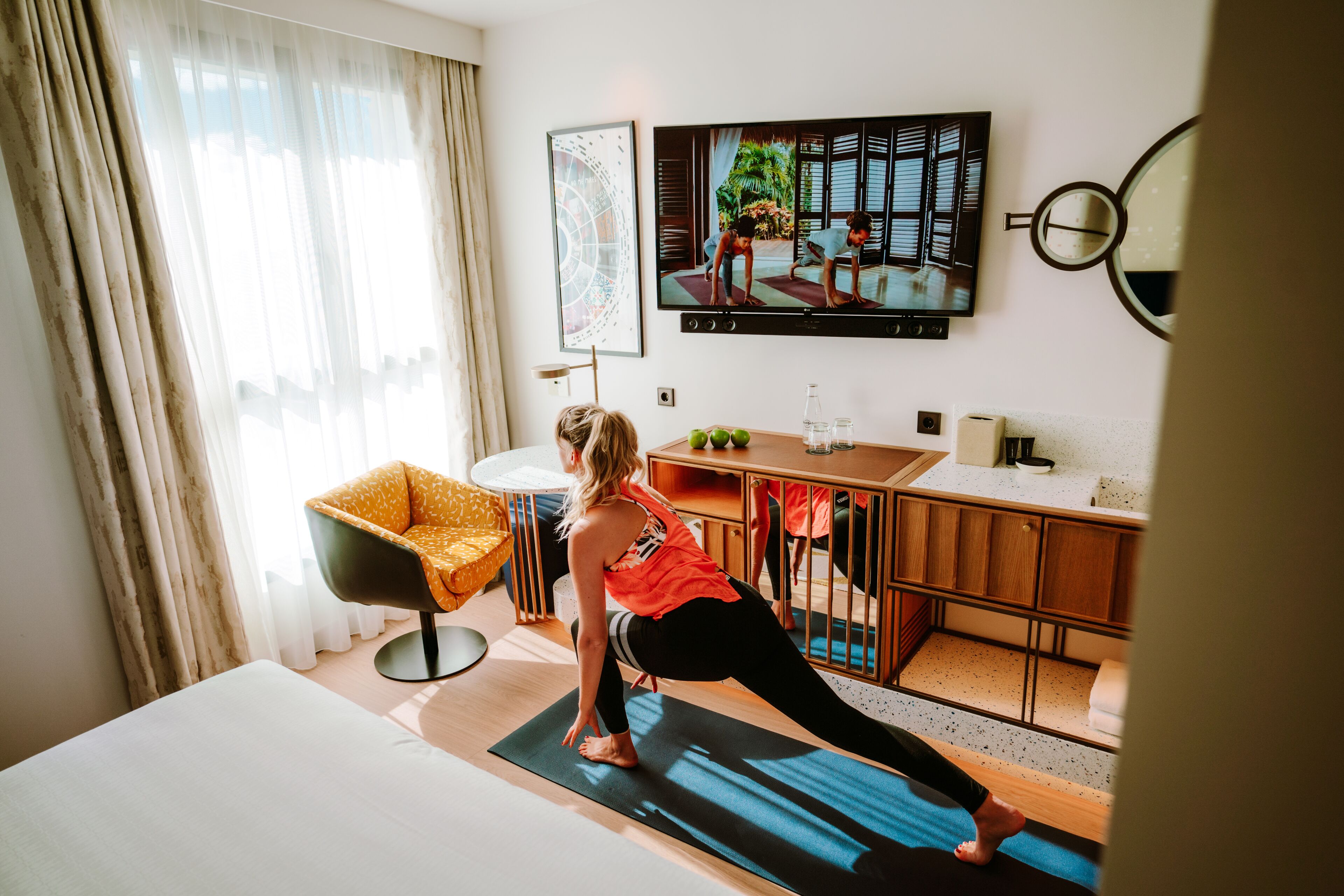 Habitación de hotel con cama, colchoneta de yoga, televisor, escritorio y silla.