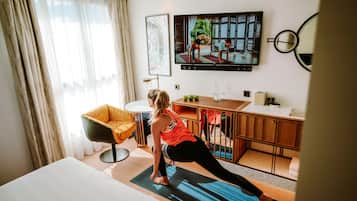 A hotel room with a bed, a yoga mat, a TV, a desk, and a chair.