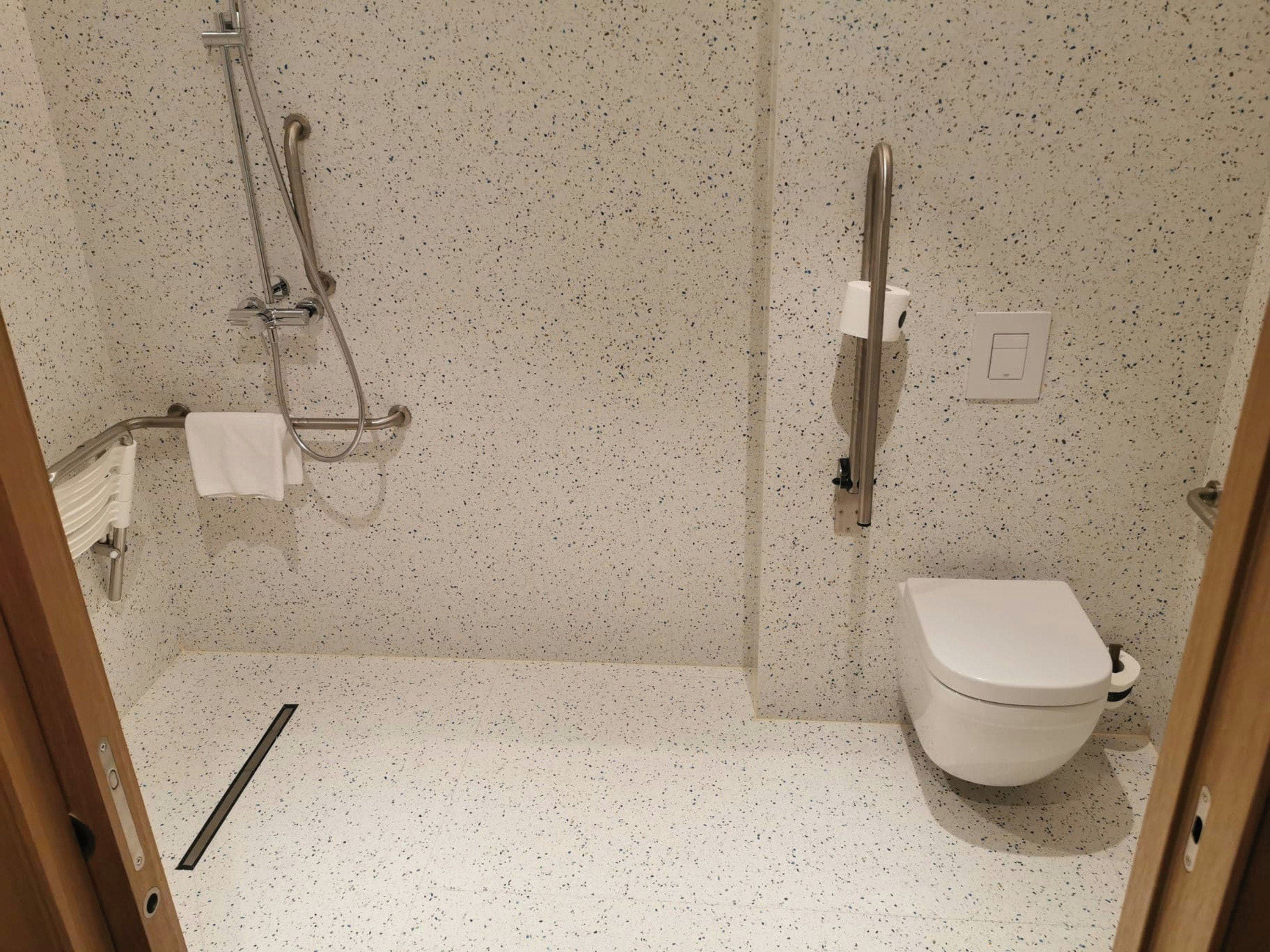 A small, compact bathroom with a shower, toilet, and a towel rack.