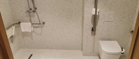 A small, compact bathroom with a shower, toilet, and a towel rack.