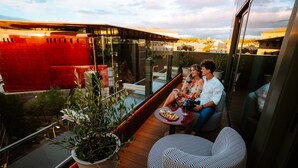 Un área de estar exterior moderna con barandilla de vidrio, plantas en macetas y vistas de la ciudad.