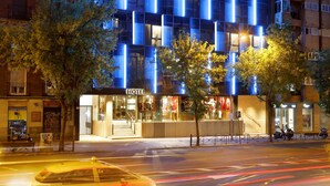Een modern hotel met een glazen gevel, verlicht met blauw licht, en een zichtbaar 'HOTEL' bord.