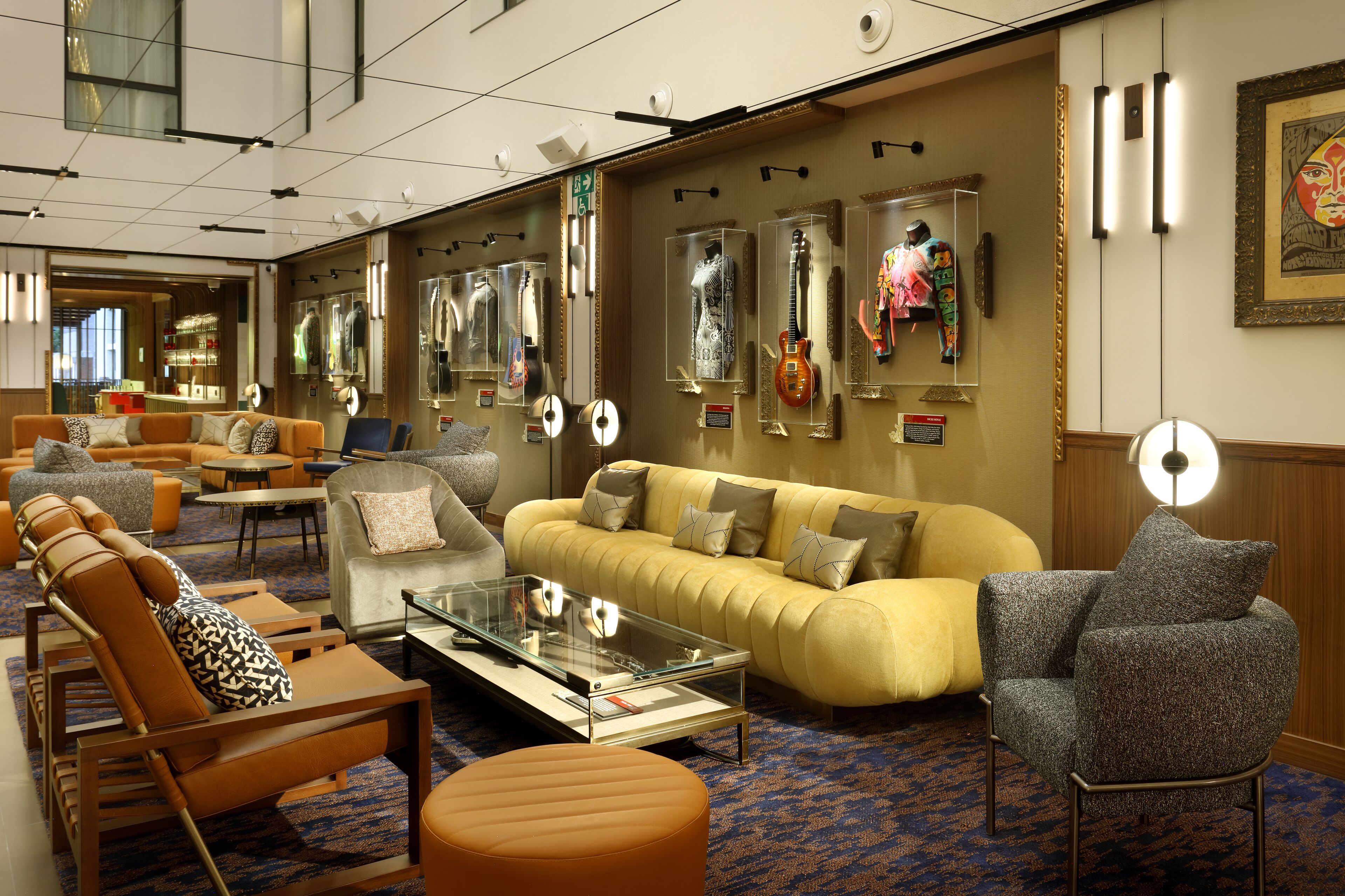 A hotel lobby with a sofa, armchairs, a coffee table, and a mirror wall displaying various items.