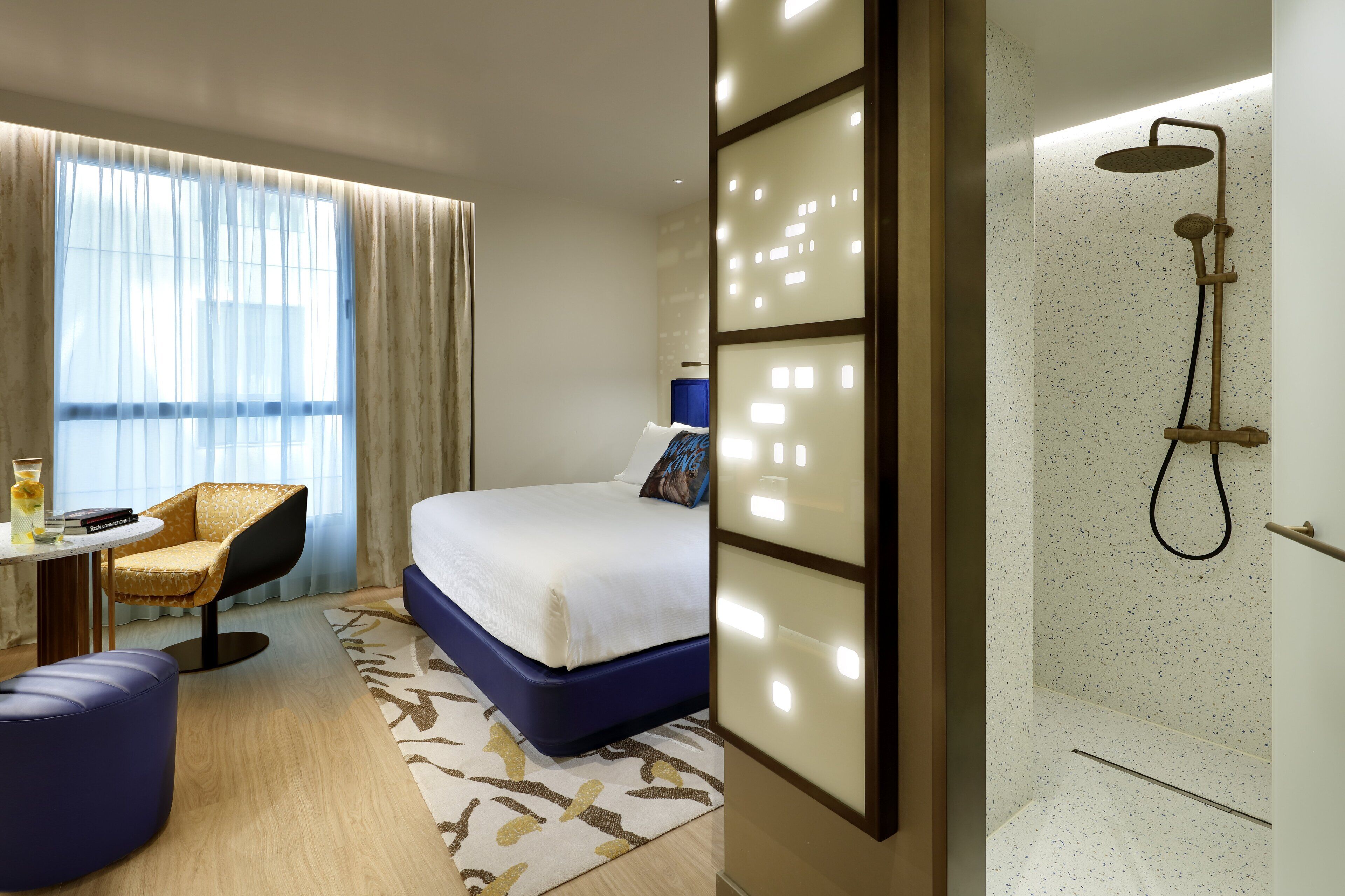 A hotel room with a bed, a chair, a table, and a shower area.