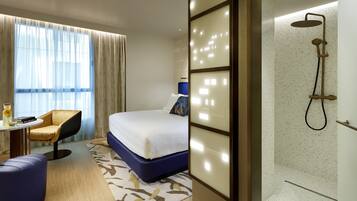 A hotel room with a bed, a chair, a table, and a shower area.