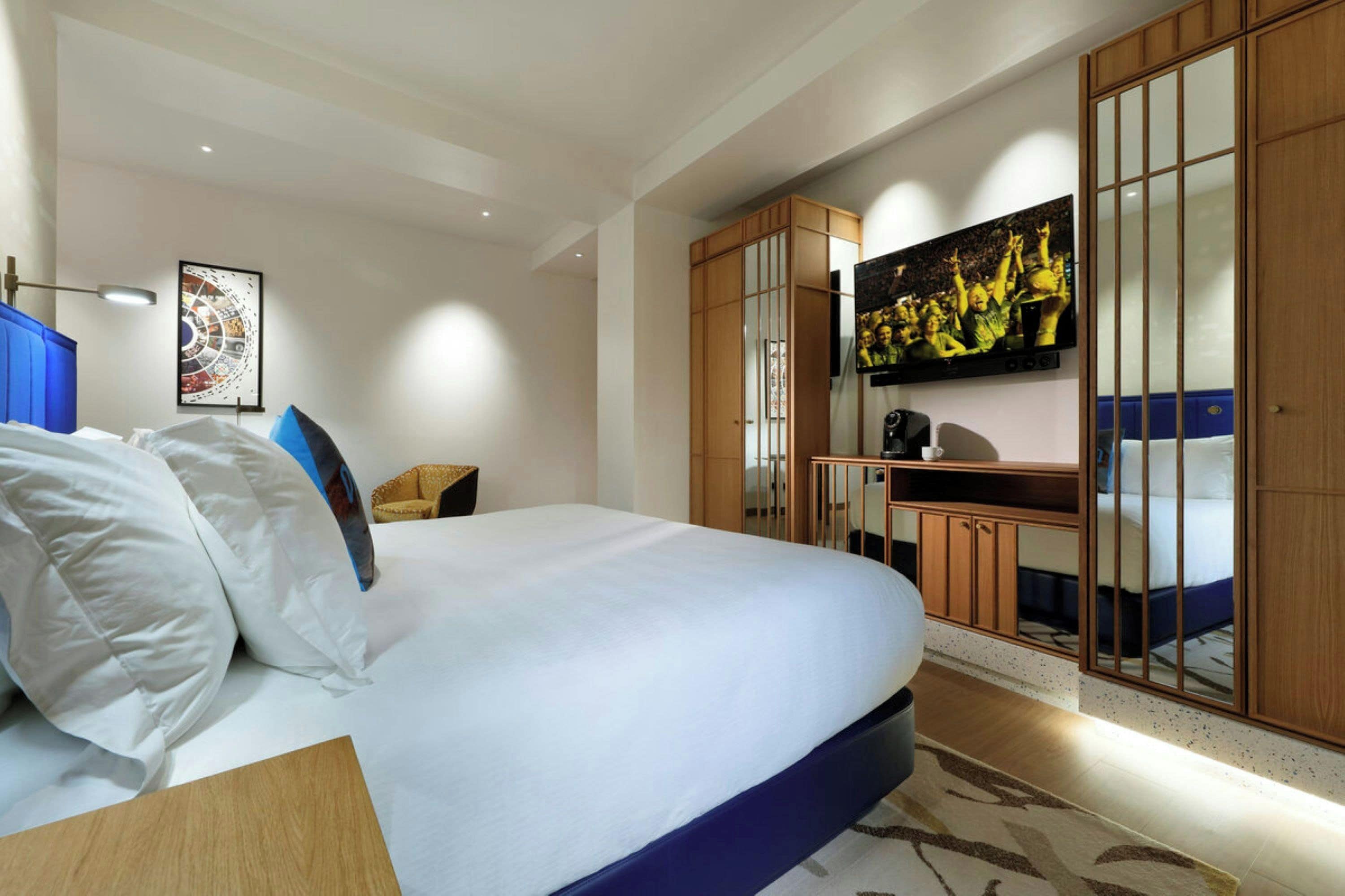 Una habitación de hotel moderna con una cama grande, un televisor de pantalla plana en la pared, un escritorio con una silla y un armario con puertas correderas.