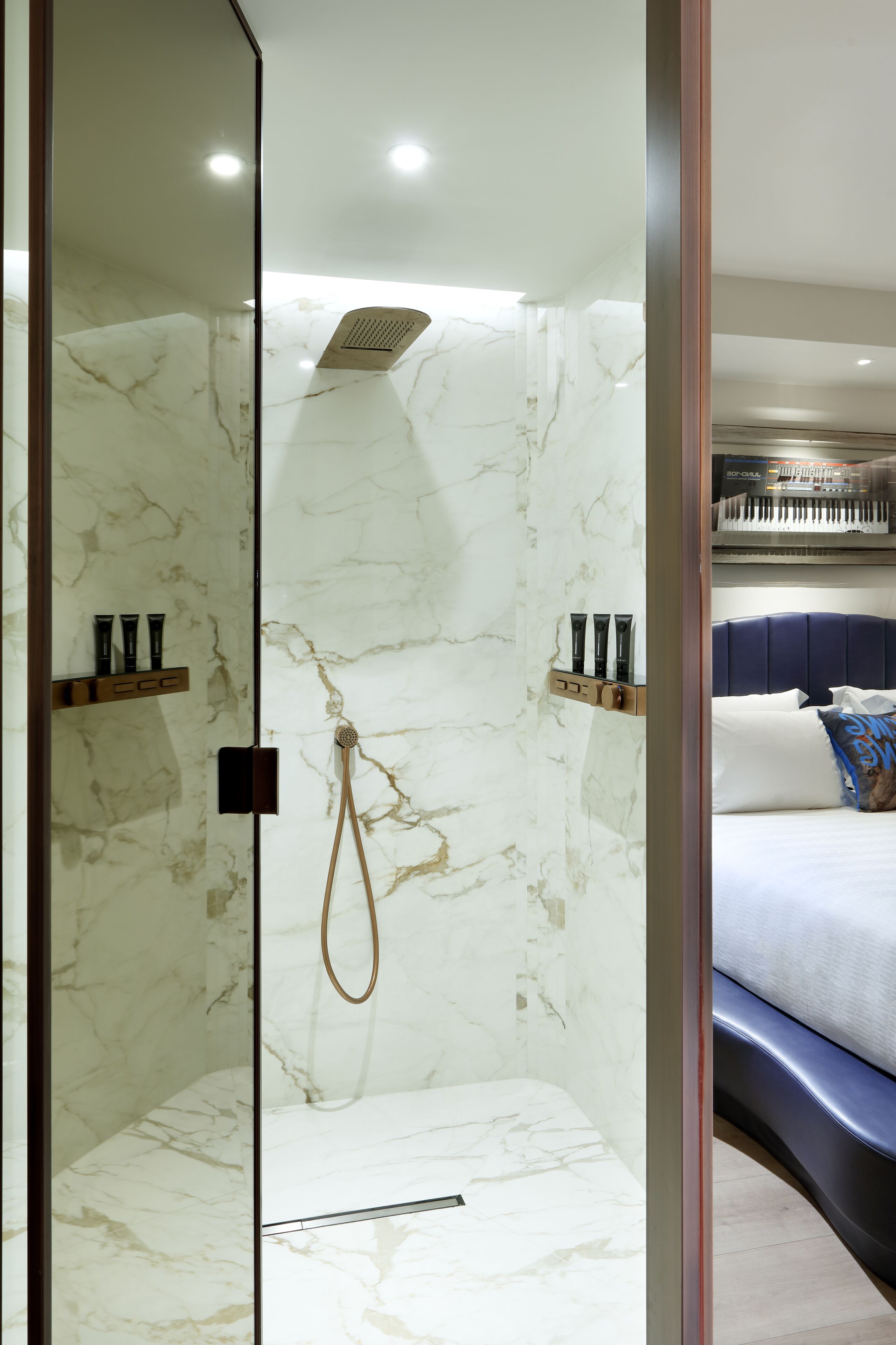 A modern bathroom with marble walls, a shower, and a bed with a blue headboard and pillows.