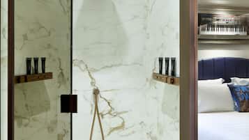 A modern bathroom with marble walls, a shower, and a bed with a blue headboard and pillows.