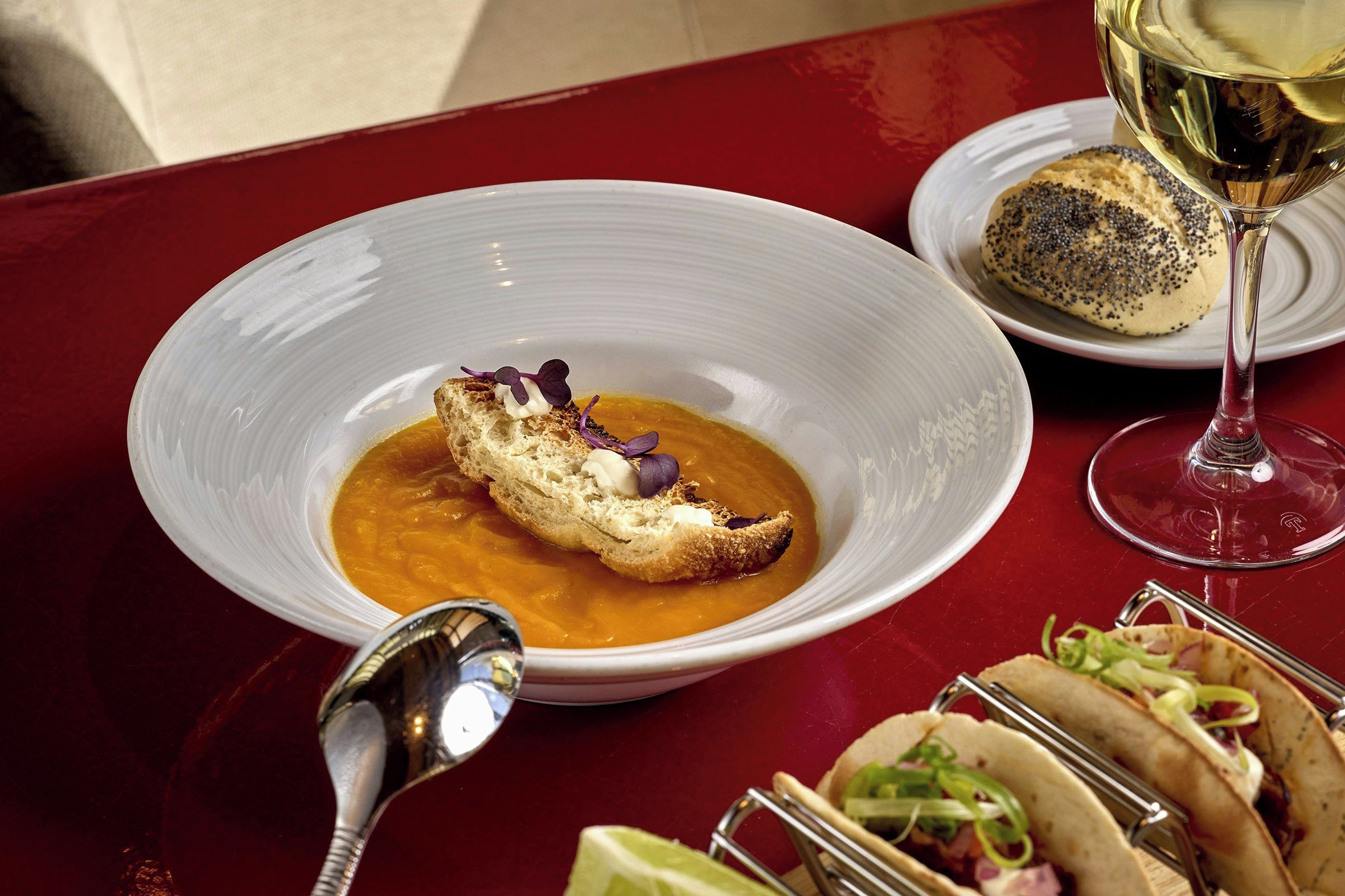 A table with a bowl of soup, a glass of wine, and tacos.