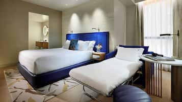 Quarto de hotel com duas camas, uma escrivaninha, uma cadeira, um espelho e uma janela com cortinas.
