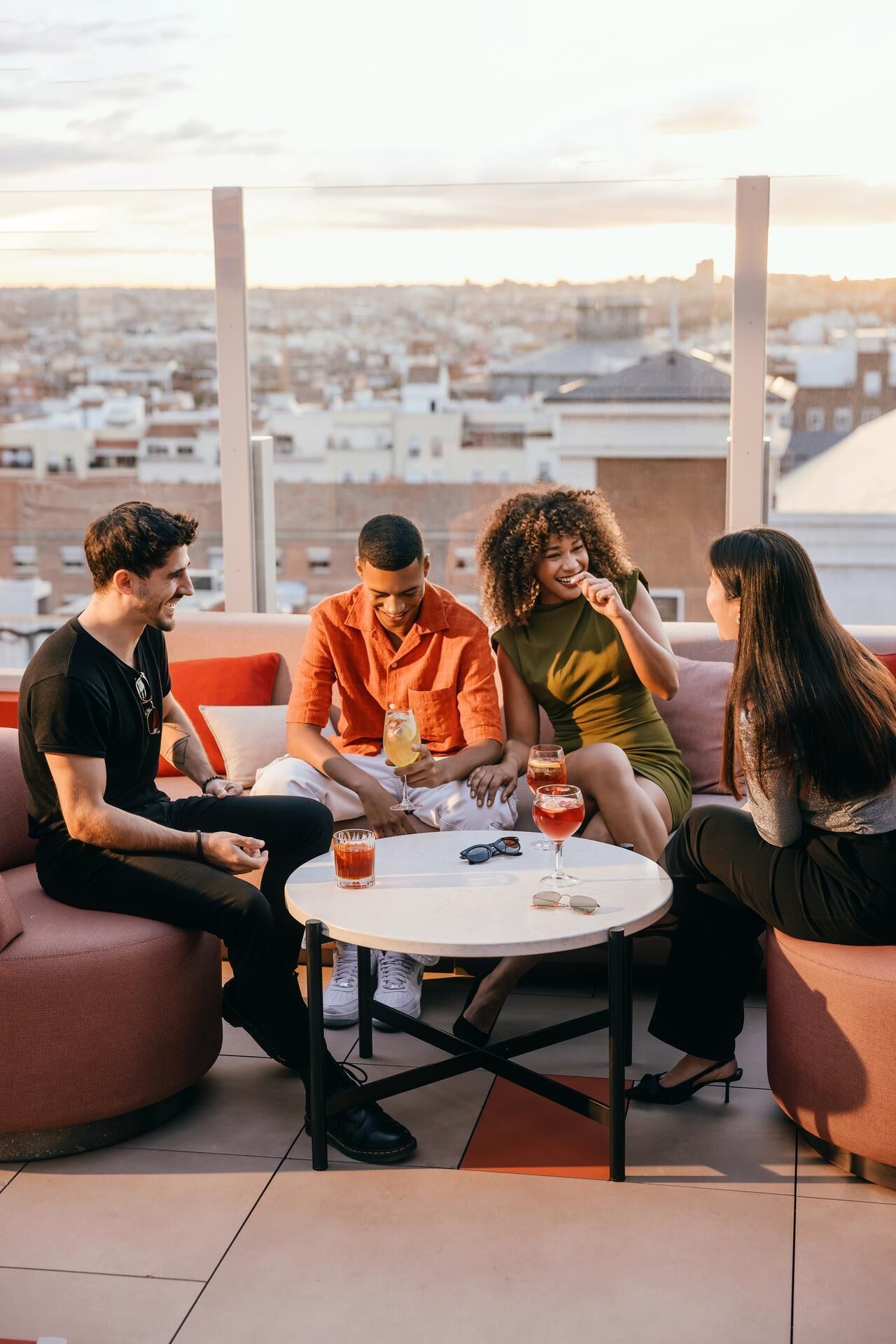 Eine Gruppe von Personen sitzt an einem runden Tisch auf einer Dachterrasse mit Blick auf die Stadt.