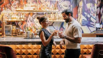 Eine Bar mit modernem Design, darunter eine Wand mit geometrischem Muster und eine Auswahl an Flaschen in Regalen.
