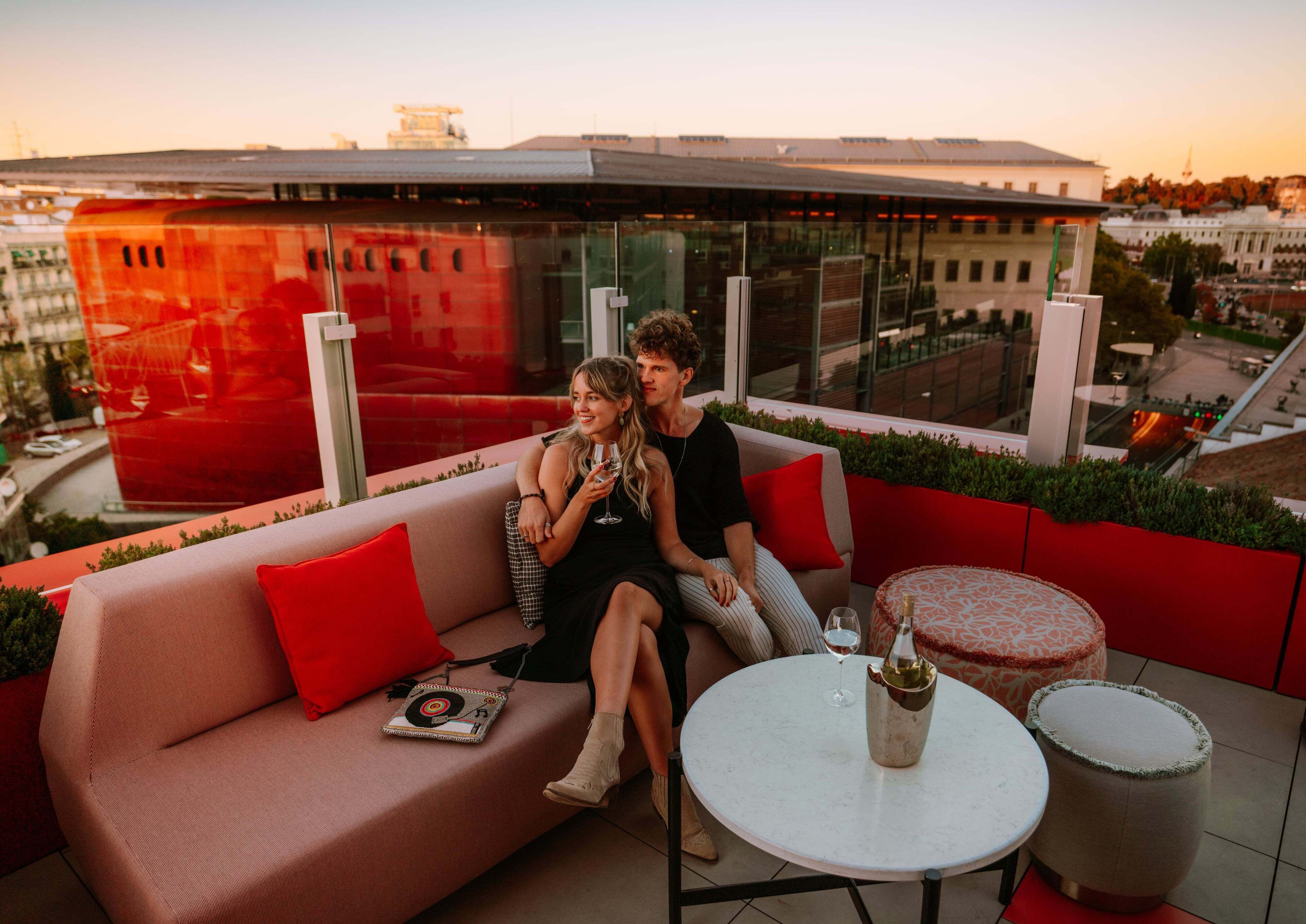 Un espace extérieur moderne aménagé avec un canapé et une table ronde, offrant une vue sur la ville en arrière-plan.