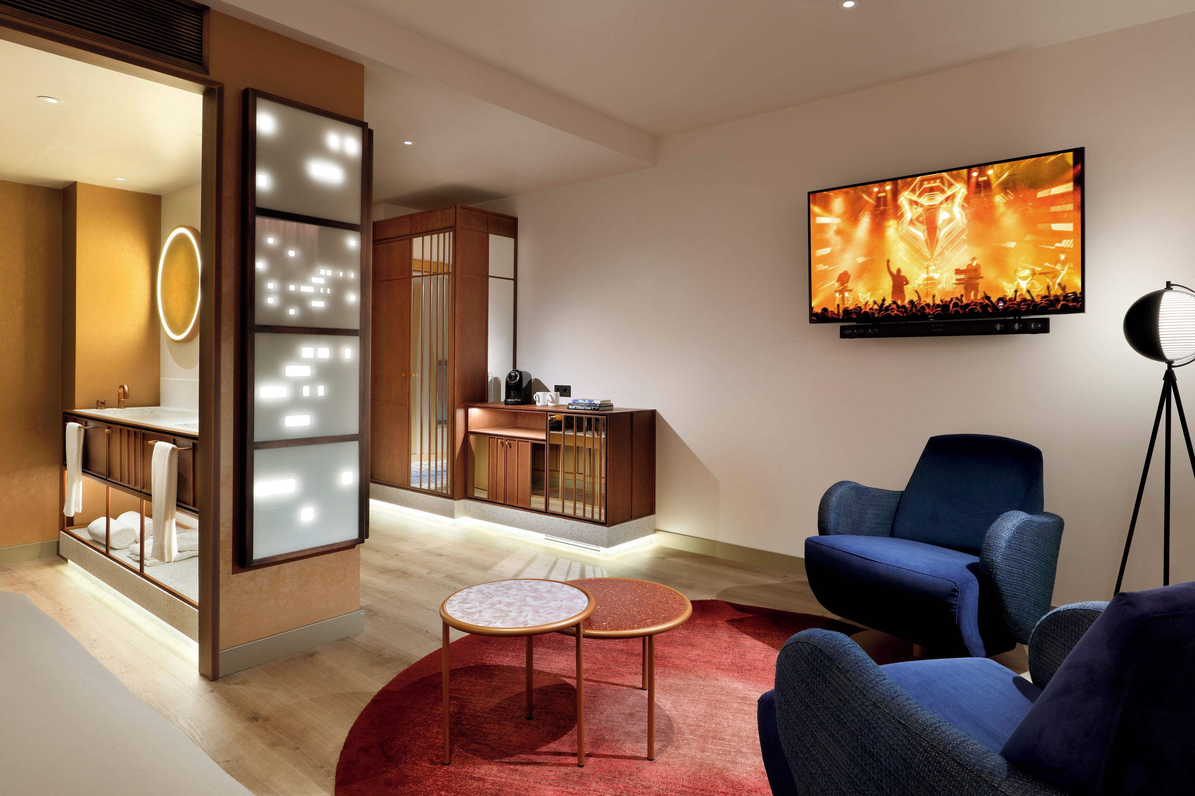Una sala de estar moderna con un televisor de pantalla plana grande, un sillón azul, una mesita redonda y una alfombra roja.