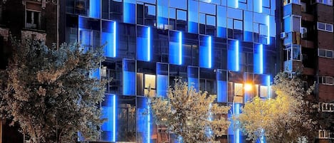 Un edificio de hotel moderno con fachada de vidrio y paneles azules iluminados.