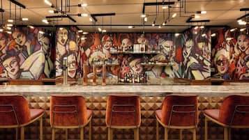 Angolo bar con un bancone in marmo, diversi sgabelli da bar e una parete decorata con dipinti astratti colorati.