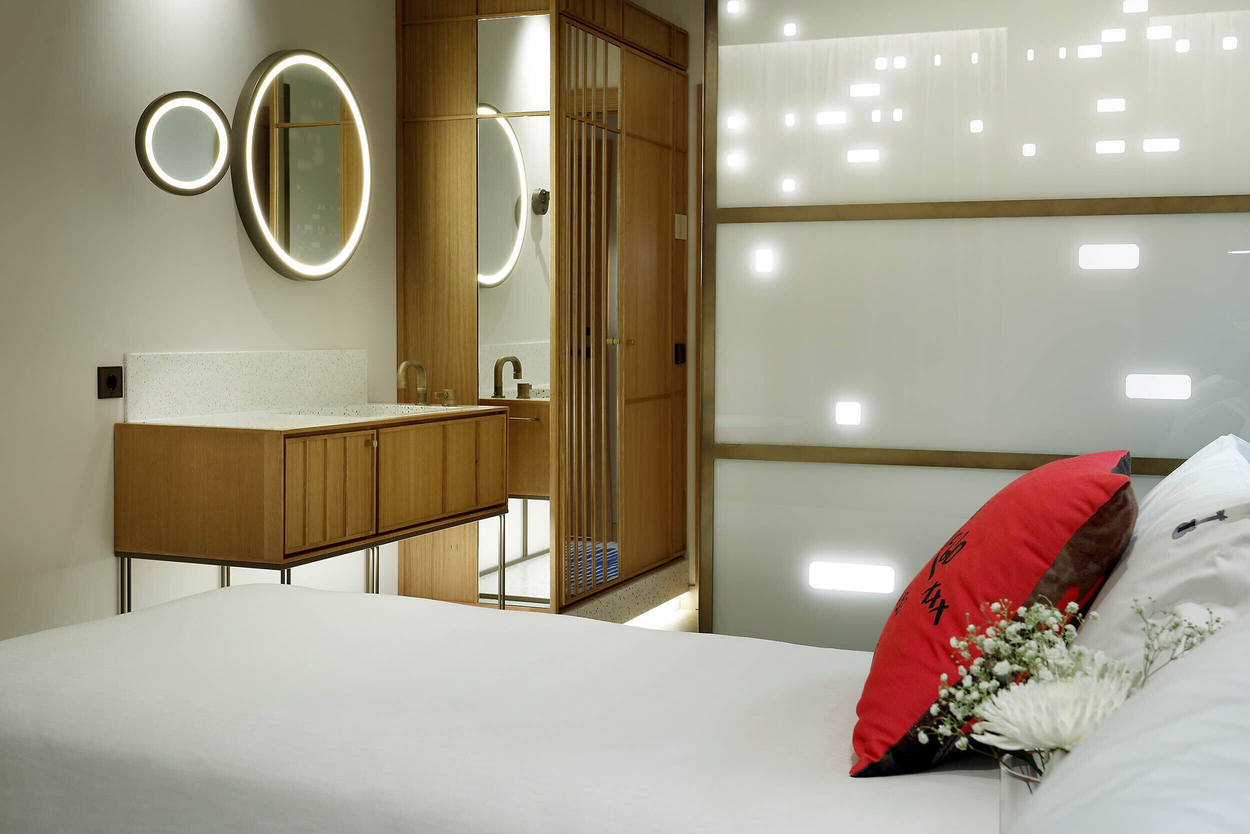 Une chambre moderne avec une coiffeuse en bois, un grand miroir et un lit agrémenté de coussins décoratifs.