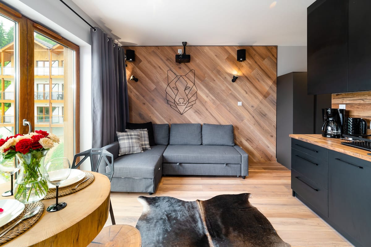 Un salon moderne avec un canapé gris, un plancher en bois et une grande fenêtre donnant sur un balcon.