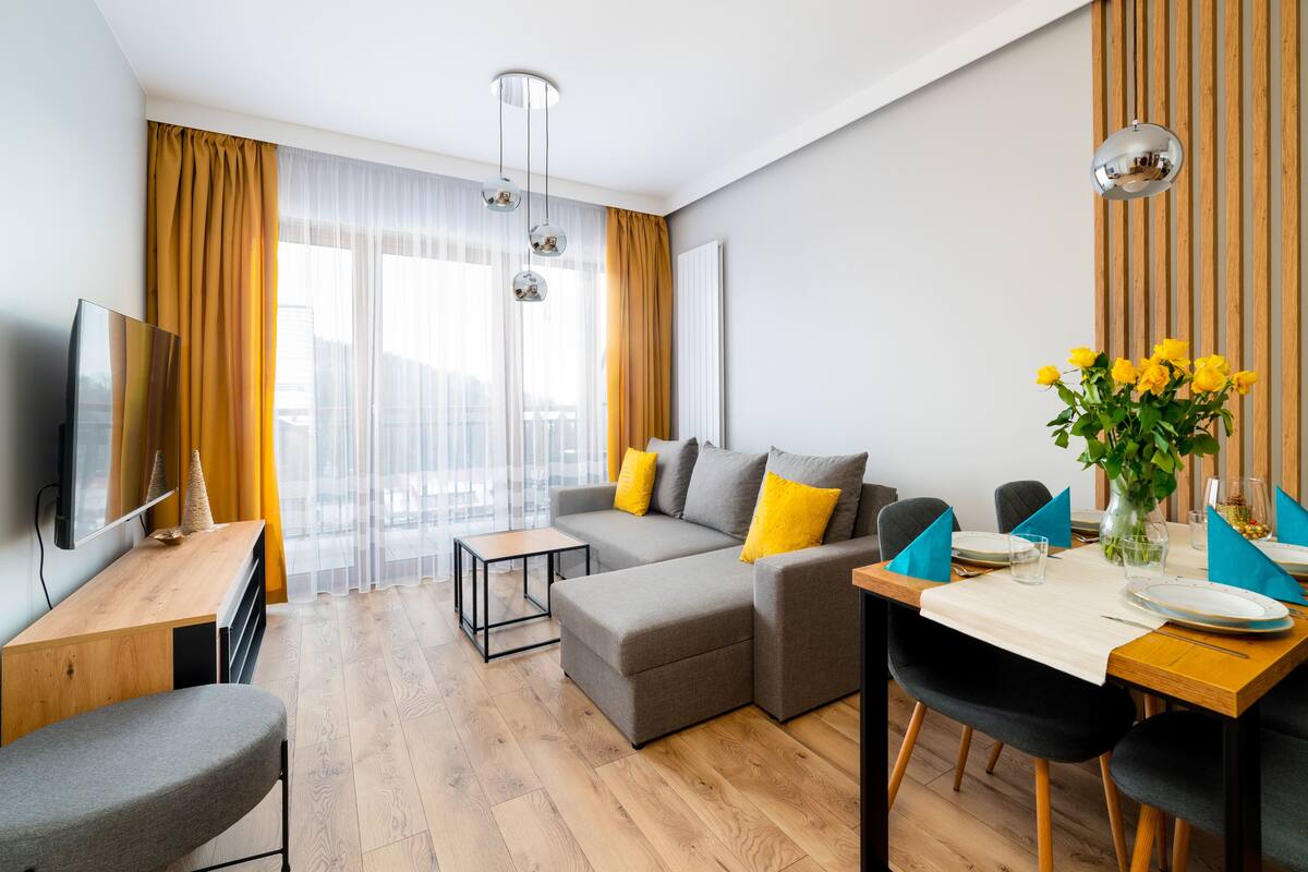 Un salon moderne avec un canapé, une table à manger dressée pour deux personnes et un téléviseur posé sur une petite table en bois.