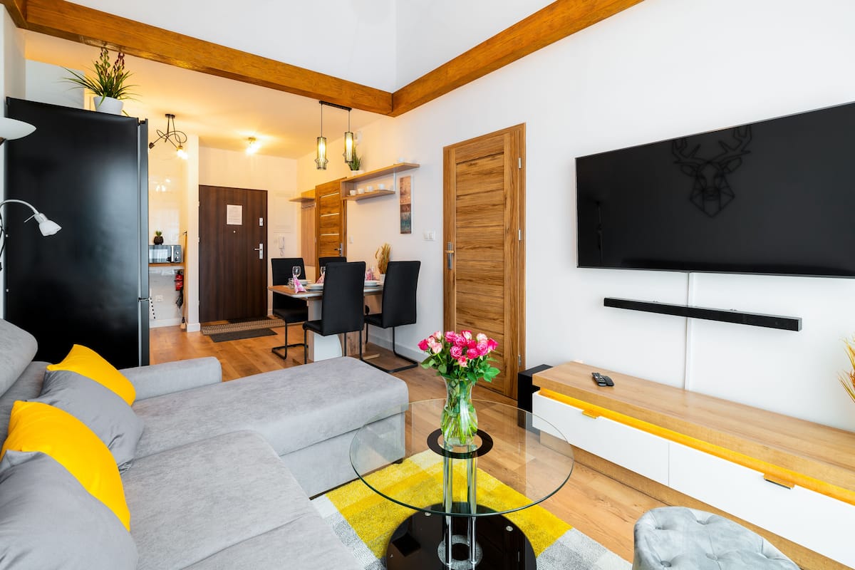 Un salon moderne avec un canapé gris, une table basse en verre et un téléviseur à écran plat fixé au mur.